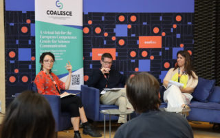 A photo of the COALESCE press conference at ESOF, showing two women sitting on the stage, flanking a man, with the heads of two members of the audience seen from behind.