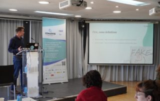 Person presenting next to a banner and screen.