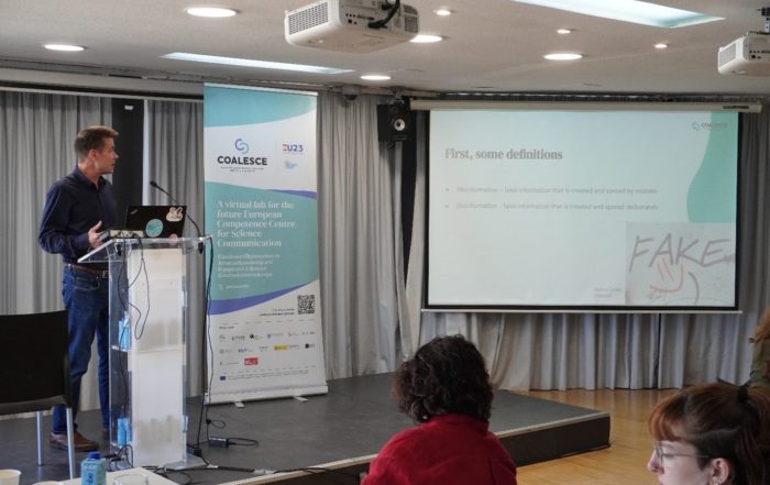 Person presenting next to a banner and screen.